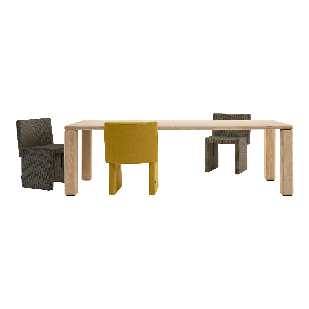 Dining table with light wood finish and modern chairs in yellow, grey, and dark grey upholstery. Stylish and contemporary design.