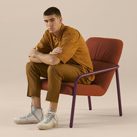 Brown and orange chair with a purple frame, styled with a beige background. Casual clothing in earthy tones.