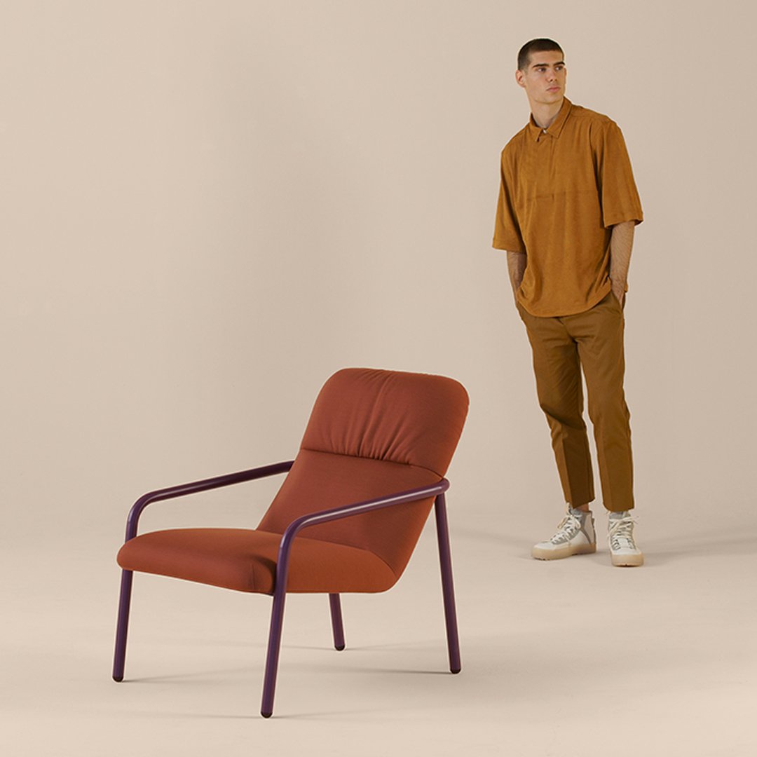 Rust orange armchair with purple metal frame, set against a neutral beige background. Modern and stylish design.