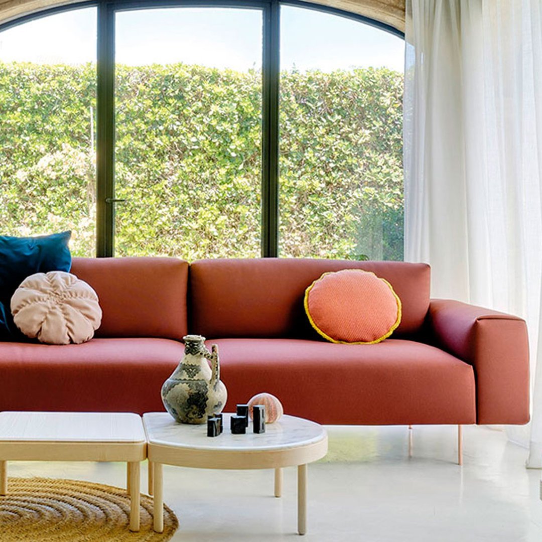 Modern terracotta sofa with vibrant pink and yellow cushions, set against a bright, airy backdrop.