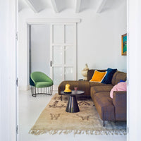 "Modern living room featuring a brown sofa, green chair, colorful cushions, and a patterned rug against a white backdrop."