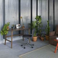 "Stylish gray desk chair on a light gray floor, surrounded by green plants and a patterned area rug in a modern space."