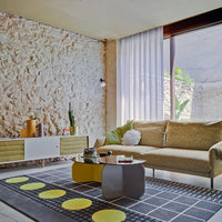 Modern living room featuring earthy tones with yellow accents, geometric patterns, and a textured stone wall.