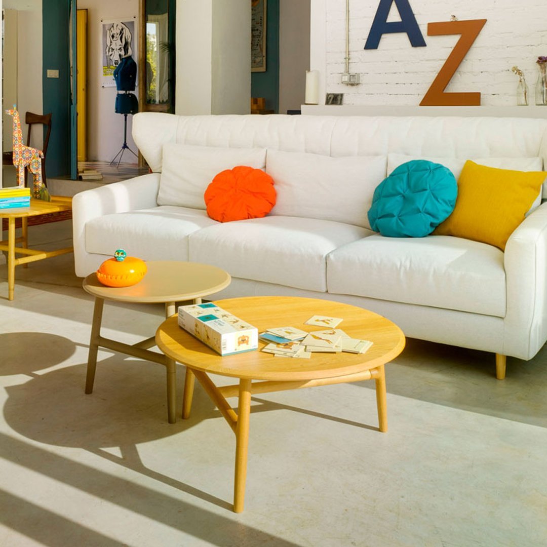 "White sofa with vibrant orange, teal, and yellow cushions; natural wood coffee tables complementing modern decor."