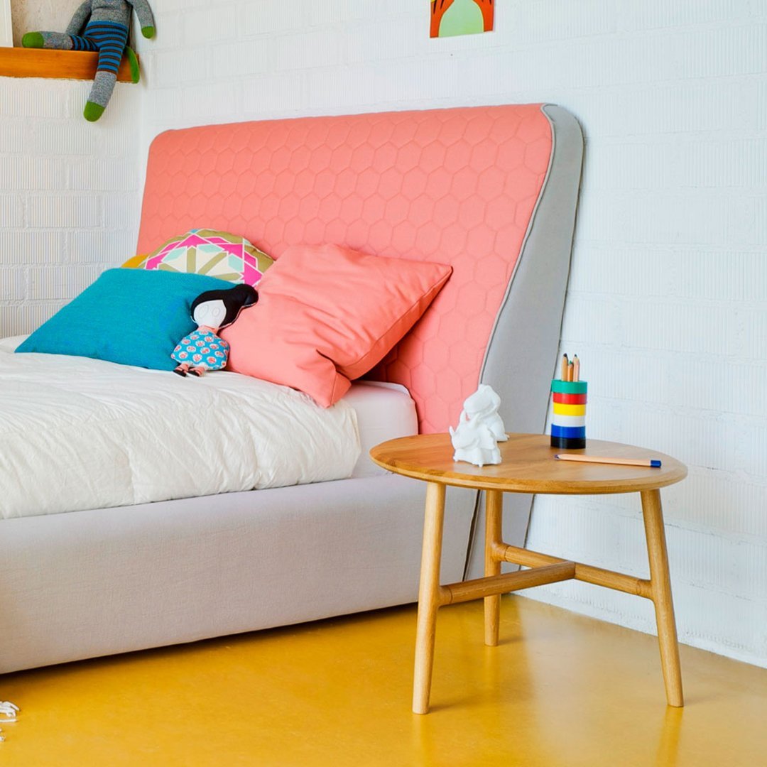 Coral pink and light gray upholstered bed with vibrant blue and green pillows, featuring a wooden side table.
