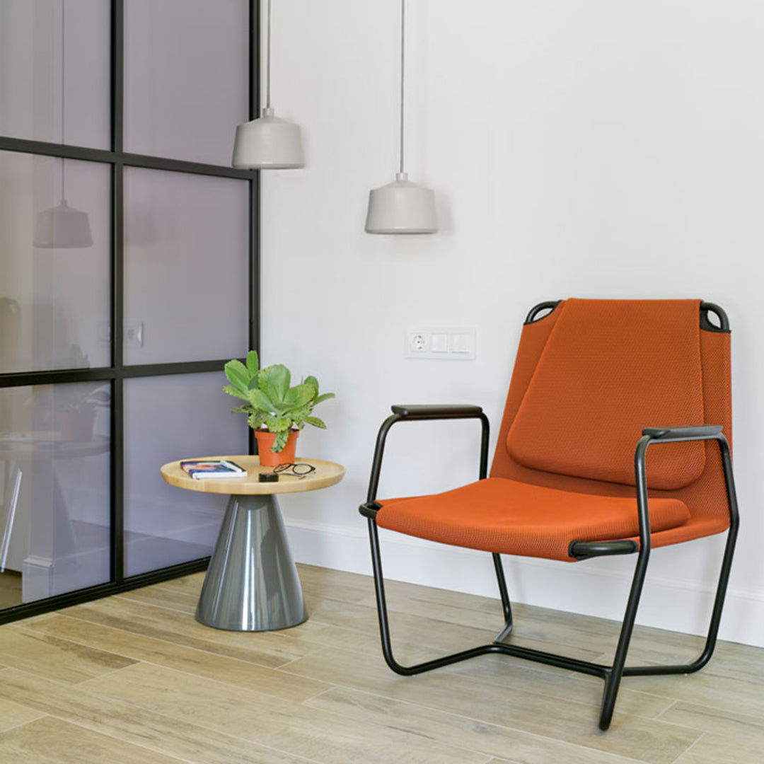 Modern orange chair with sleek black frame, paired with a round wood and metal table against a minimalist backdrop.