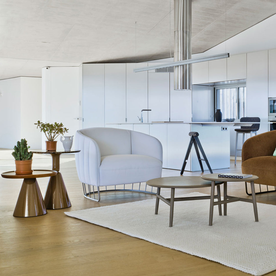 Modern living room featuring a white curved chair, brown tables, and natural tones in a stylish open layout.
