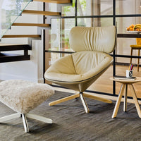 Cream leather accent chair with a sleek design, complemented by a fluffy white ottoman and light wooden side table.