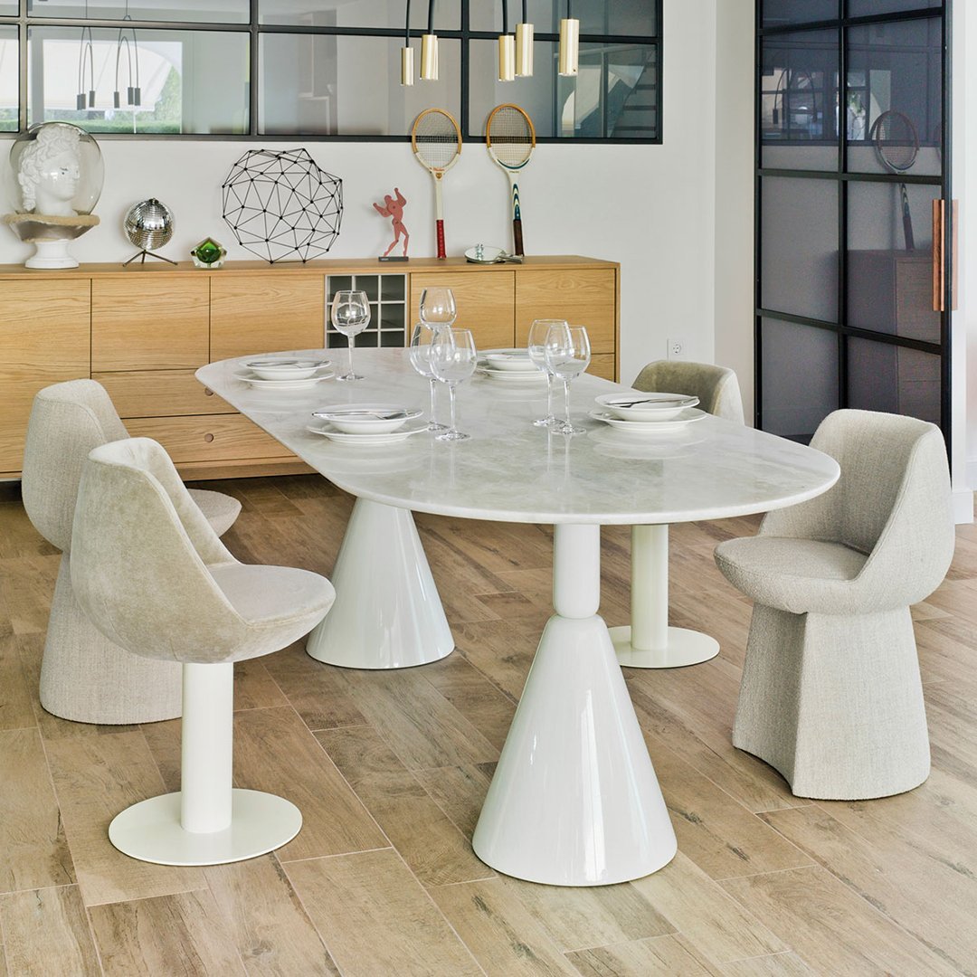 Modern dining table with a smooth white marble top and sculptural white bases, accompanied by beige upholstered chairs.