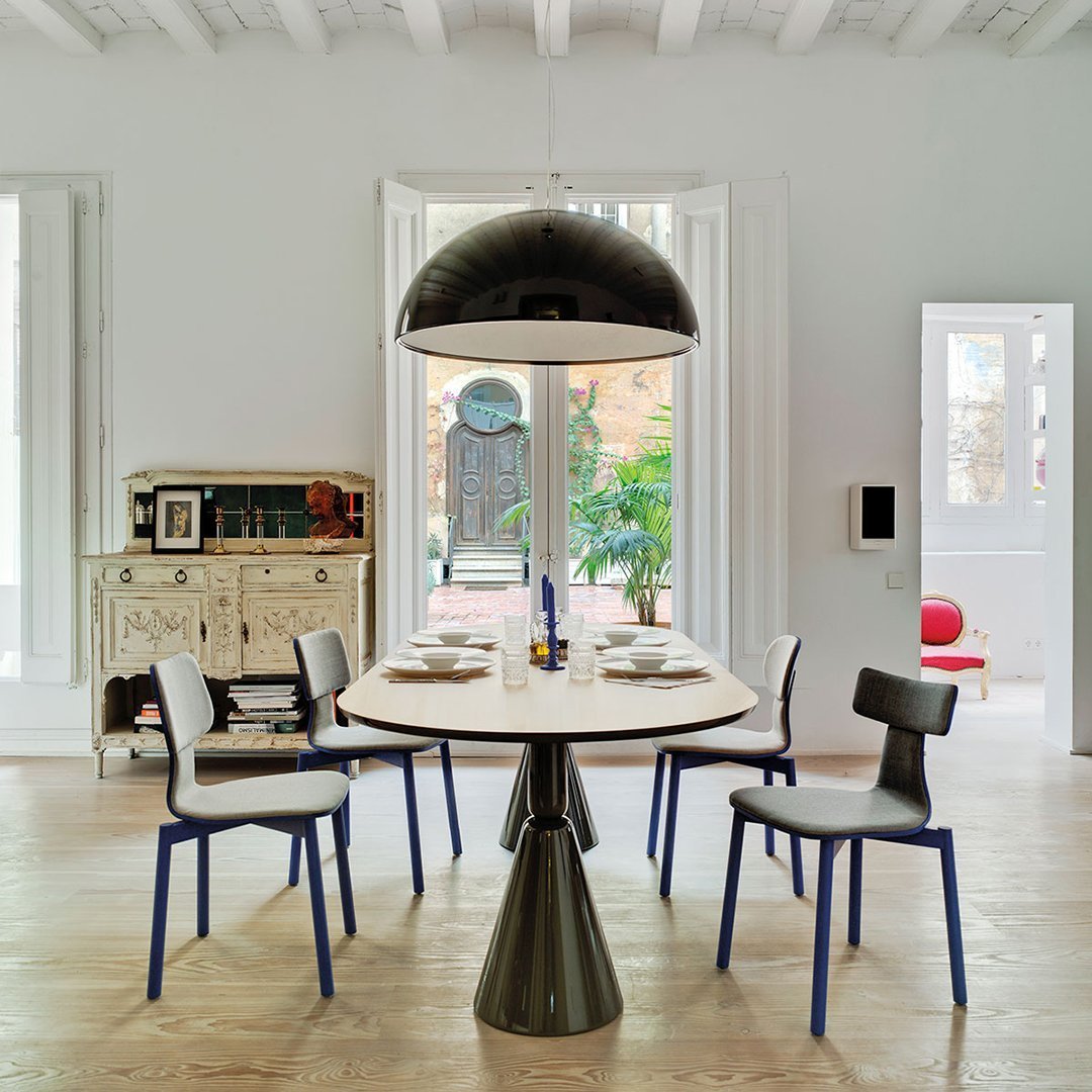 Modern dining room featuring a round white table, black dome pendant light, and blue-accented chairs on light wood flooring.