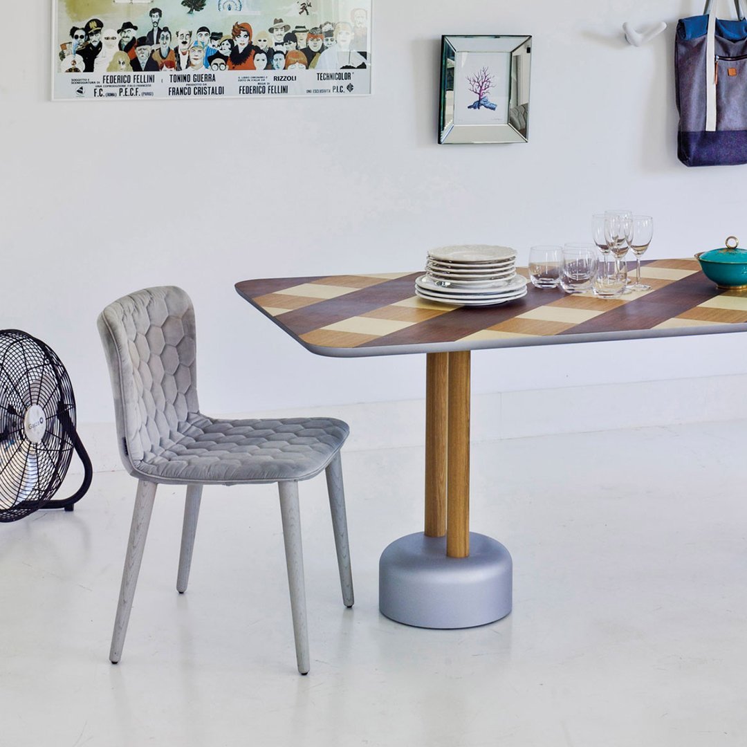 "Gray patterned chair next to a brown and beige checkered dining table on a light floor."