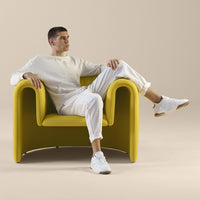 Bright yellow chair with smooth curves, paired with a neutral-toned outfit and white sneakers.