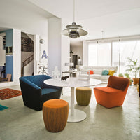 "Modern living room featuring a blue chair, orange and yellow stools, and a white round table against a neutral backdrop."