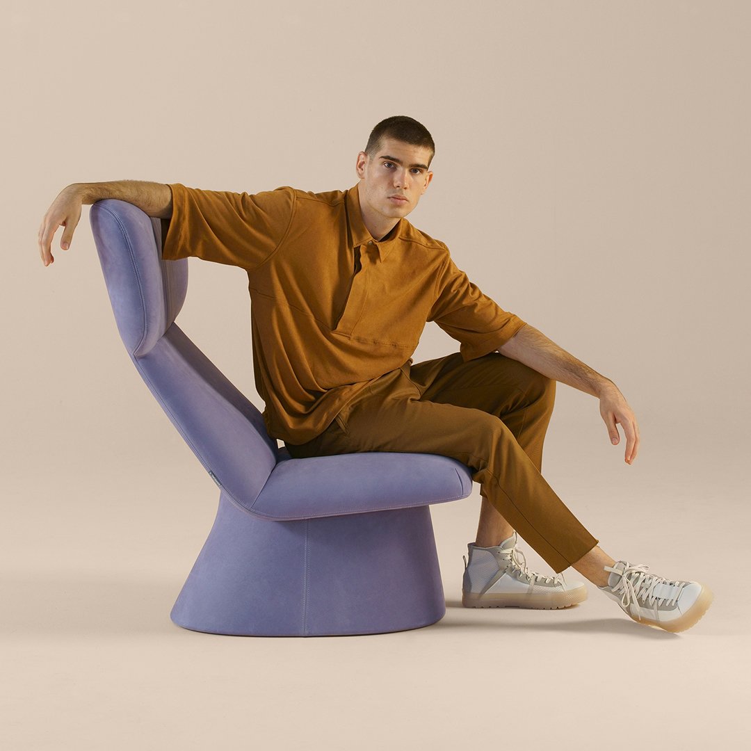 Lavender chair with smooth curves, paired with a rich brown outfit, soft textures, and neutral backdrop. Stylish and modern.