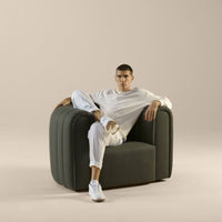 Stylish gray upholstered armchair with smooth, rounded shapes on a soft beige background. Modern aesthetic.