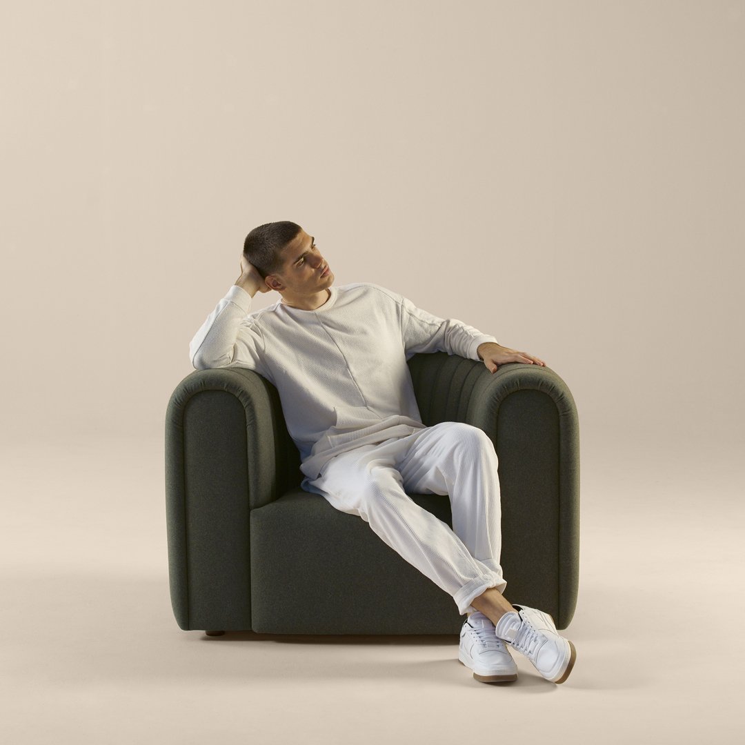 Green upholstered armchair with a smooth, modern design, paired with a neutral beige background.
