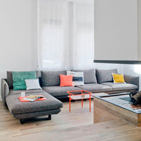 Gray sectional sofa with colorful cushions in teal, orange, and yellow, set against a bright, minimalistic room.
