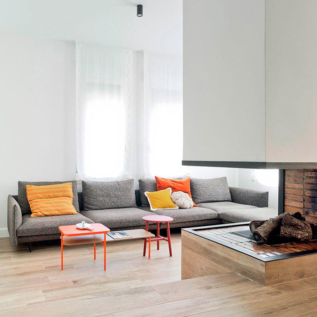 Modern gray sofa with vibrant orange and yellow cushions, paired with lively orange accent tables in a bright, airy space.