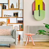 Colorful geometric wall art in green, pink, yellow; soft gray sofa; light wood flooring; white shelves with assorted decor.