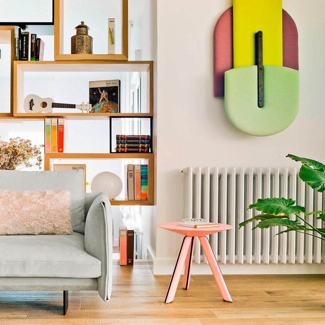 Soft gray sofa, pastel pink table, vibrant green wall decor, and colorful bookshelf create a modern, inviting living space.
