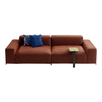 Brown modular sofa with textured fabric, accented by a blue throw pillow and a small green side table.