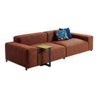 Modern orange sofa with textured fabric, featuring a blue patterned throw pillow and a green side table.