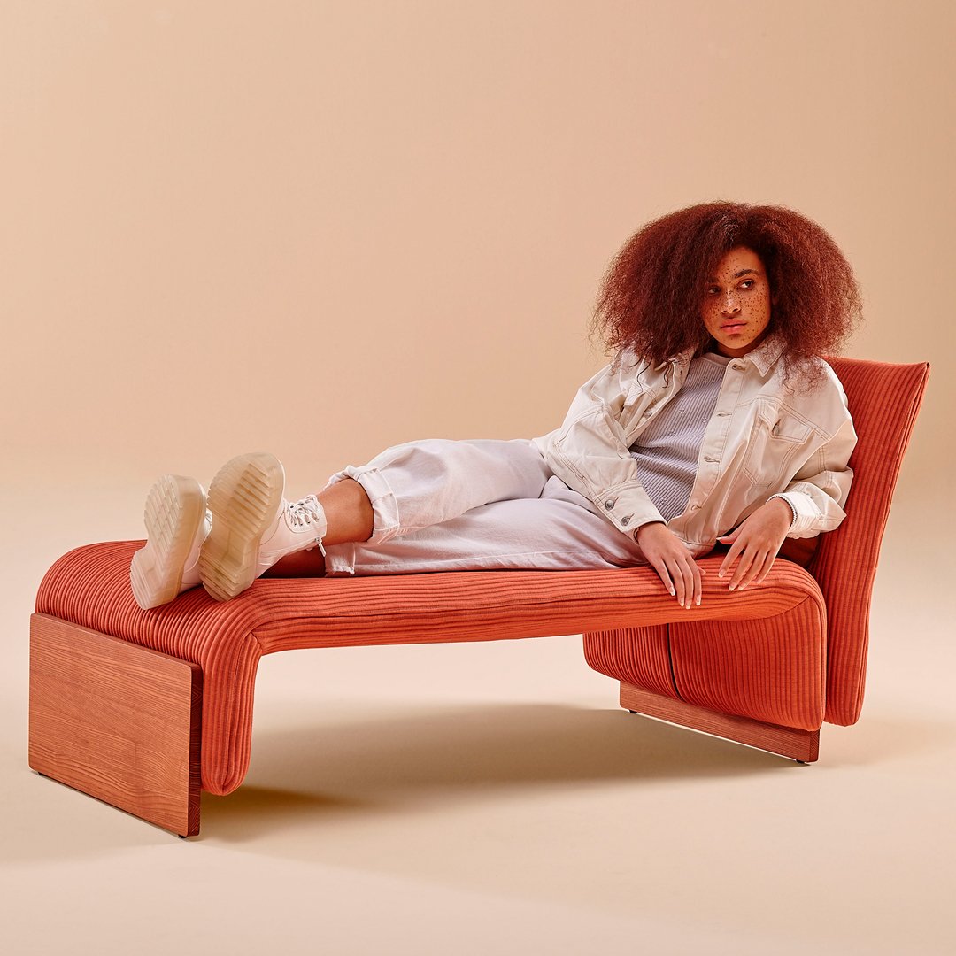 Rust-colored lounge chair with ribbed pattern and natural wood accents, set against a soft beige background.