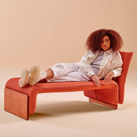 Rust-colored lounge chair with ribbed pattern and natural wood accents, set against a soft beige background.