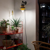 Modern wall lamp with a yellow shade, paired with green potted plants and a vibrant red shelving unit.