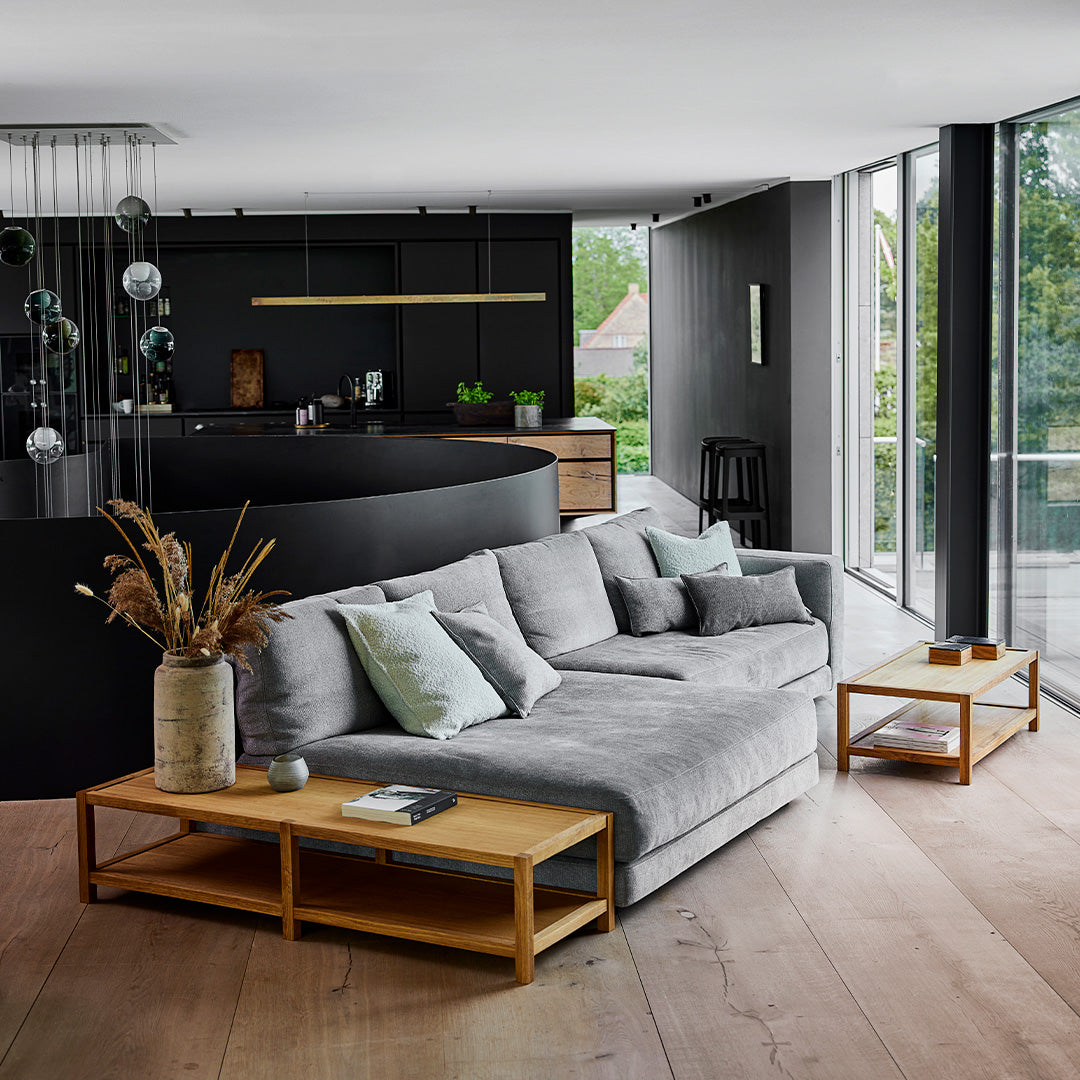 Gray sectional sofa with light blue and green pillows, complemented by wood accents and a modern black backdrop.