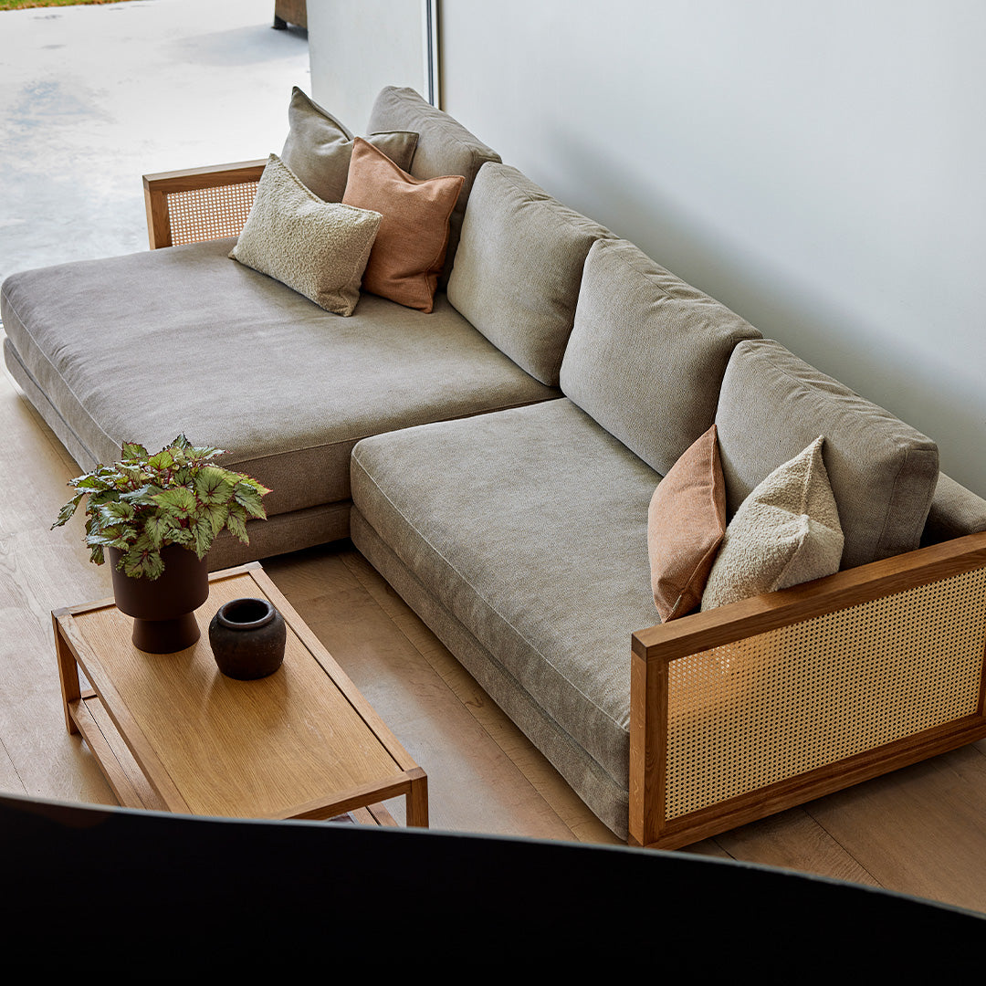 Modern gray sofa with beige and terracotta accent pillows, featuring natural wood armrests and a minimalistic design.
