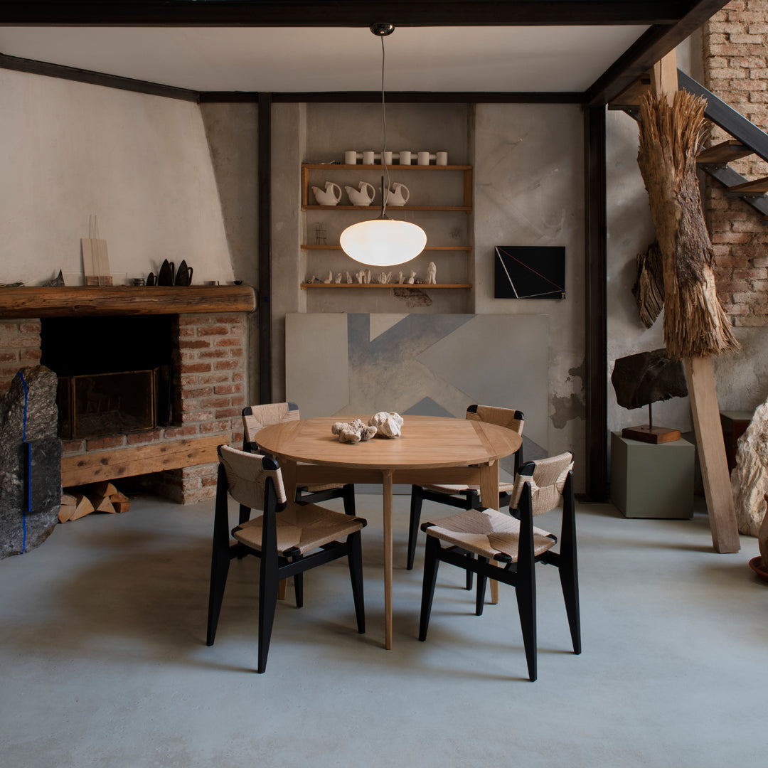 Natural wood round table with black chairs, set in a minimalist interior featuring neutral tones and organic textures.