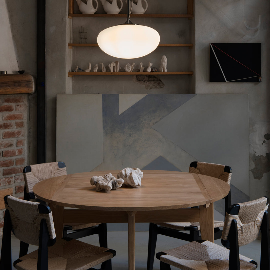 Round wooden dining table with black and natural chairs, set against a muted gray and blue abstract wall.