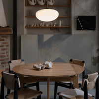 Round wooden dining table with black and natural chairs, set against a muted gray and blue abstract wall.