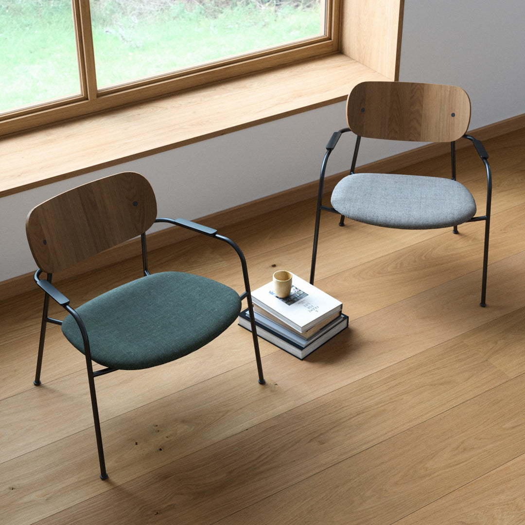 "Two modern chairs in green and gray upholstery with wooden backs, set on a light wood floor near a window."