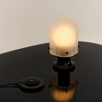 Frosted glass lamp with ridged texture, black base, and circular switch on a glossy black surface.