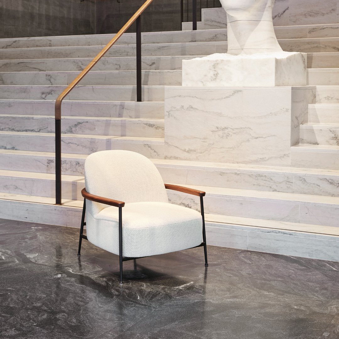 Elegant cream armchair with wooden accents, set against a sleek marble backdrop and dark stone floor.