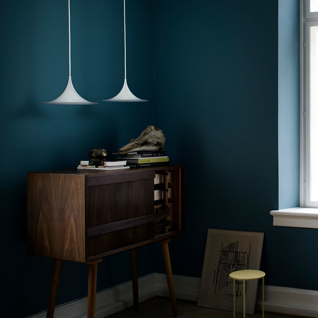 Modern walnut cabinet against deep blue wall, featuring sleek white pendant lights and a pop of yellow stool.