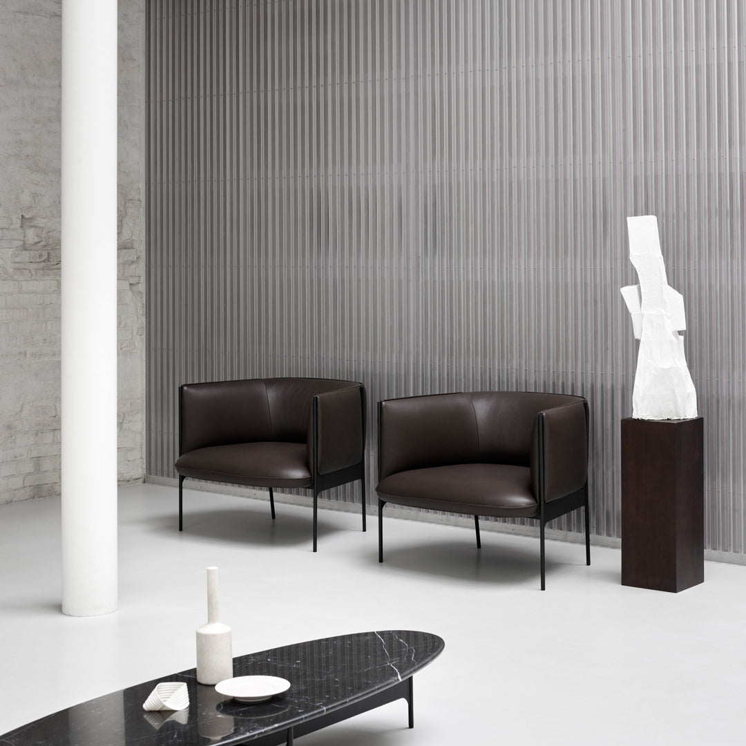 "Two dark brown leather chairs against a textured gray-striped wall, with a sleek black coffee table."