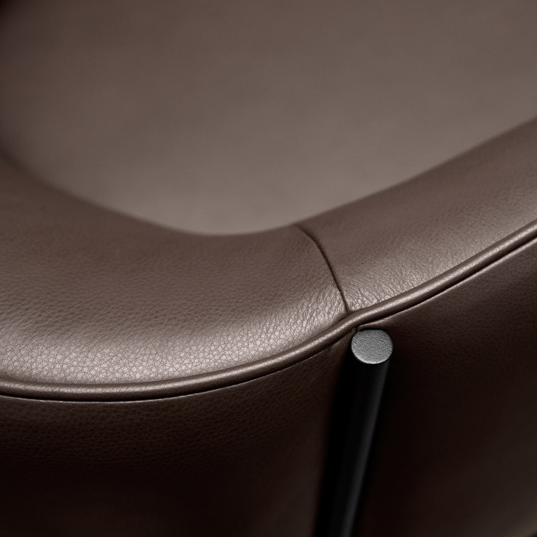 Brown leather chair close-up with smooth texture and contrasting black metal leg. Modern and stylish design.