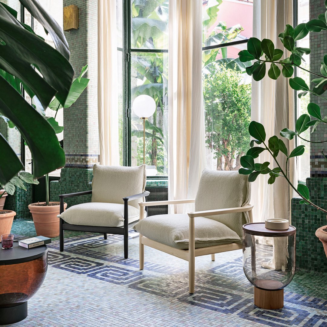Light beige and black chairs with a geometric patterned blue tile floor, surrounded by green plants and natural light.