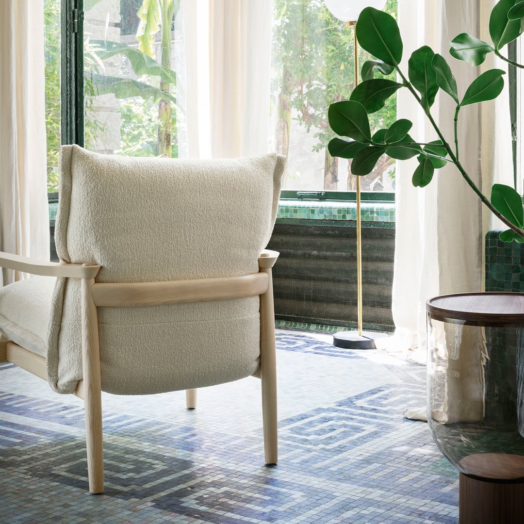 Neutral cream chair with natural wood frame, set against a blue geometric patterned rug and green plant accents.