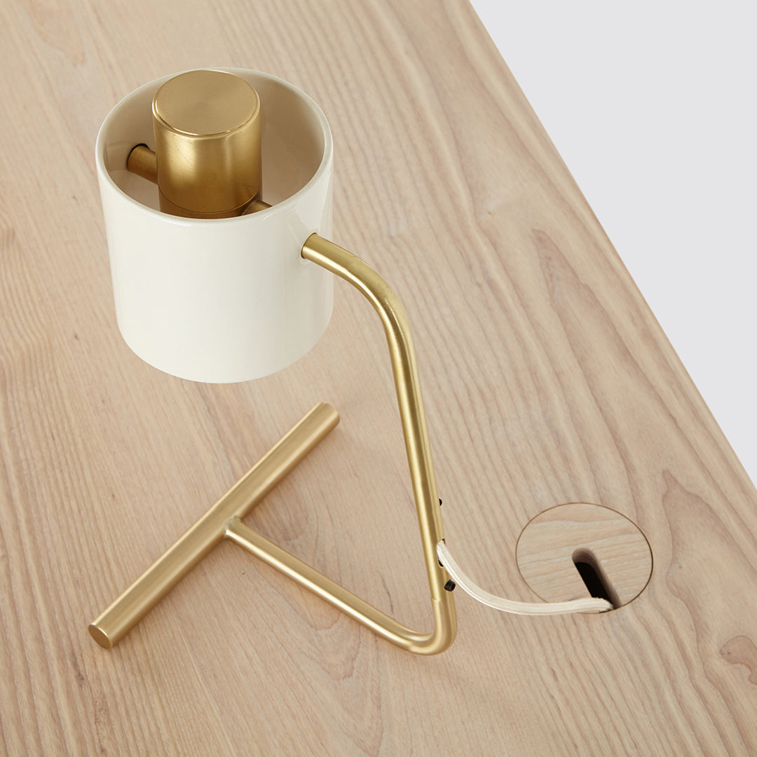White lamp with a sleek gold base and arm, featuring a minimalist design on a light wood surface.