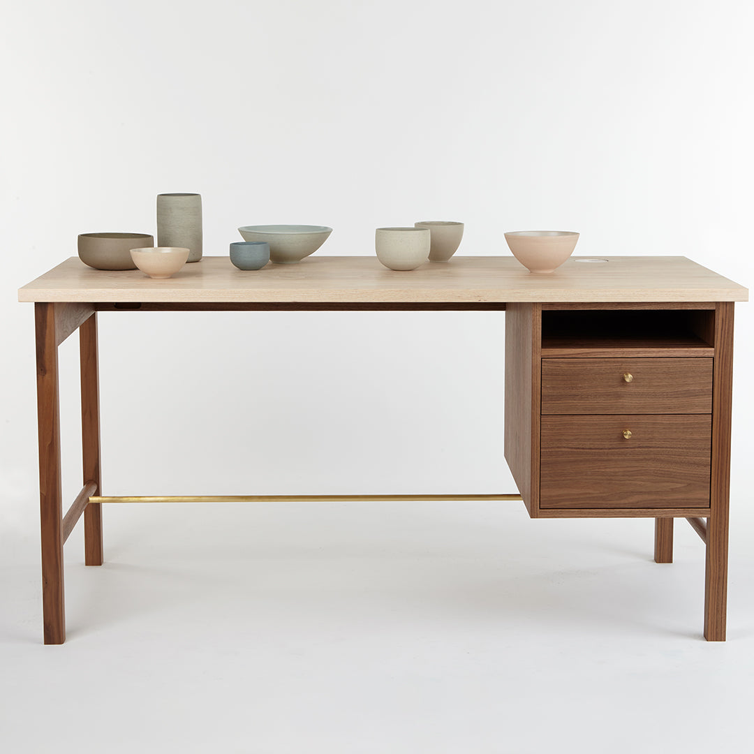 Natural wood desk with light finish and dark wood drawer; ceramic bowls in muted greens and pinks arranged decoratively.