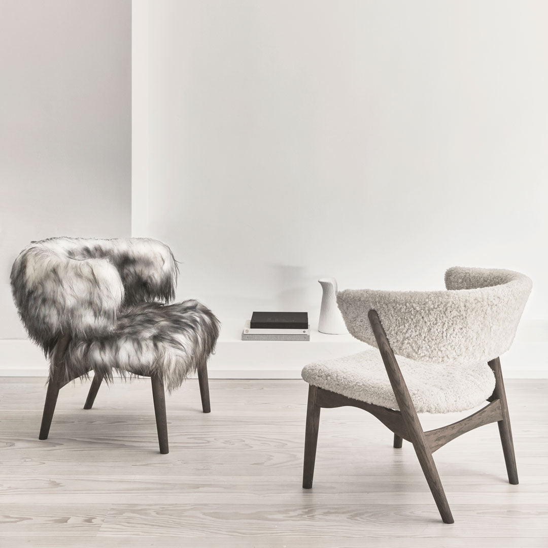 Two stylish chairs: one with gray and white faux fur, the other in soft cream, set against a minimalist backdrop.