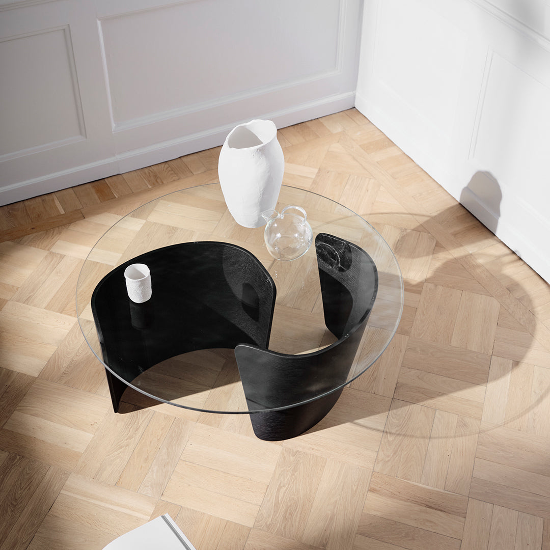 Modern round coffee table with a sleek black base and clear glass top, featuring smooth curves and minimalist design.