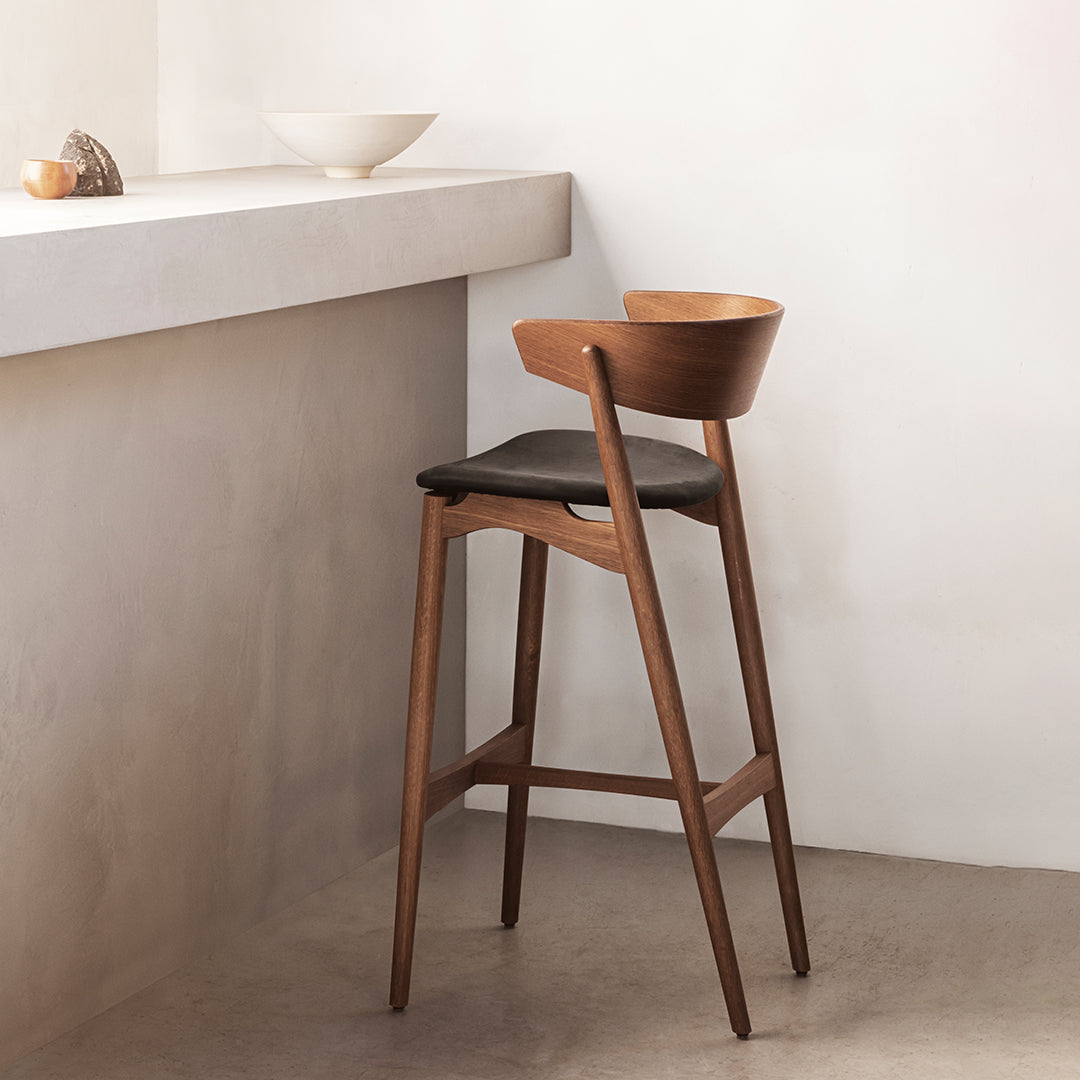 "Modern wooden bar stool in rich walnut finish with black leather seat, elegant curved backrest, minimalistic design."