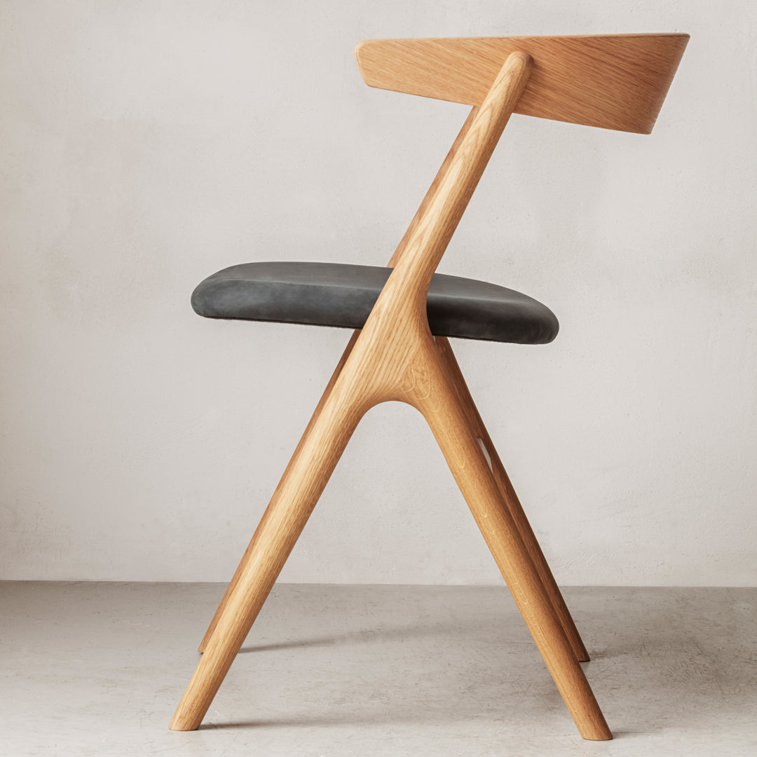 Modern wooden chair with a light oak frame and sleek black upholstered seat, featuring clean lines and minimalist design.