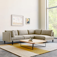 Beige sectional sofa with textured upholstery, paired with a minimalist black metal coffee table and a geometric yellow rug.