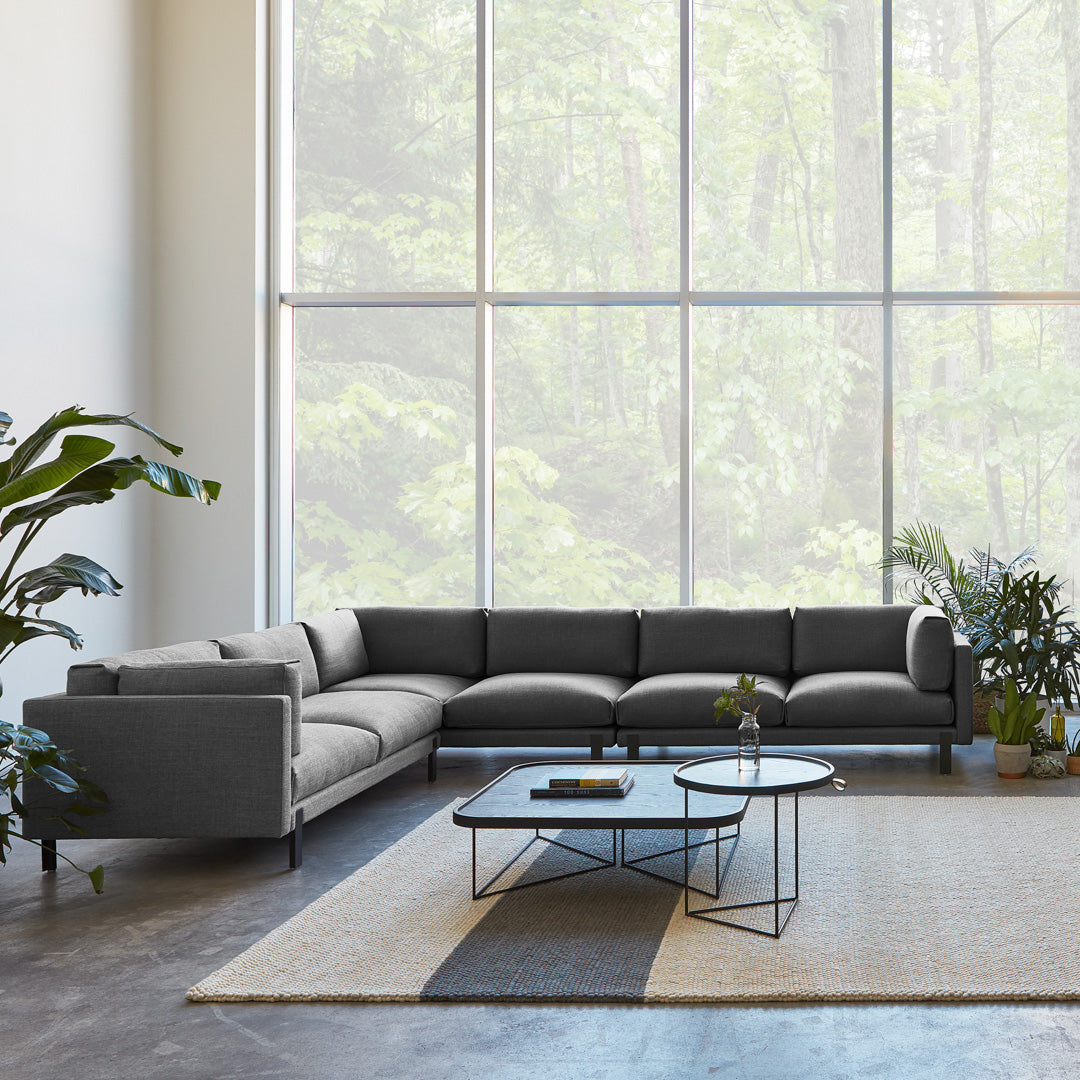 Modern gray sectional sofa with sleek lines, paired with a minimalist black metal coffee table on a neutral patterned rug.